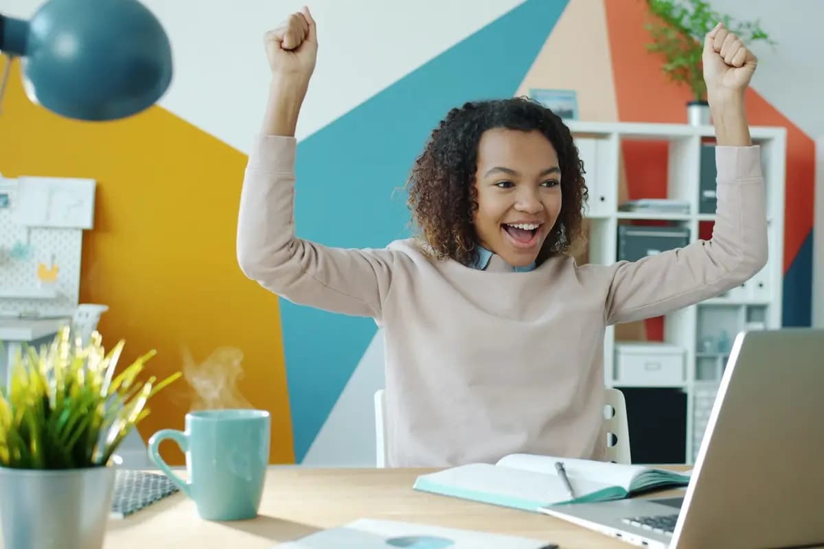 Una mujer celebra con los brazos en alto frente a su laptop.